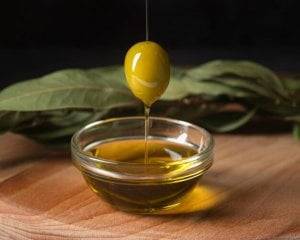 Olive suspended above bowl of olive oil